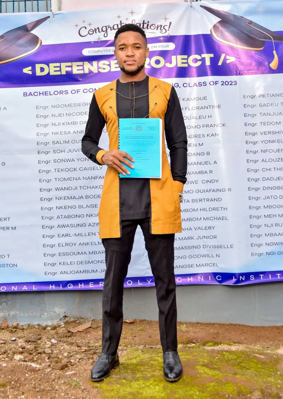 Nsom Emmanuel holding his bound thesis in front of the Class of 2023 project defence banner