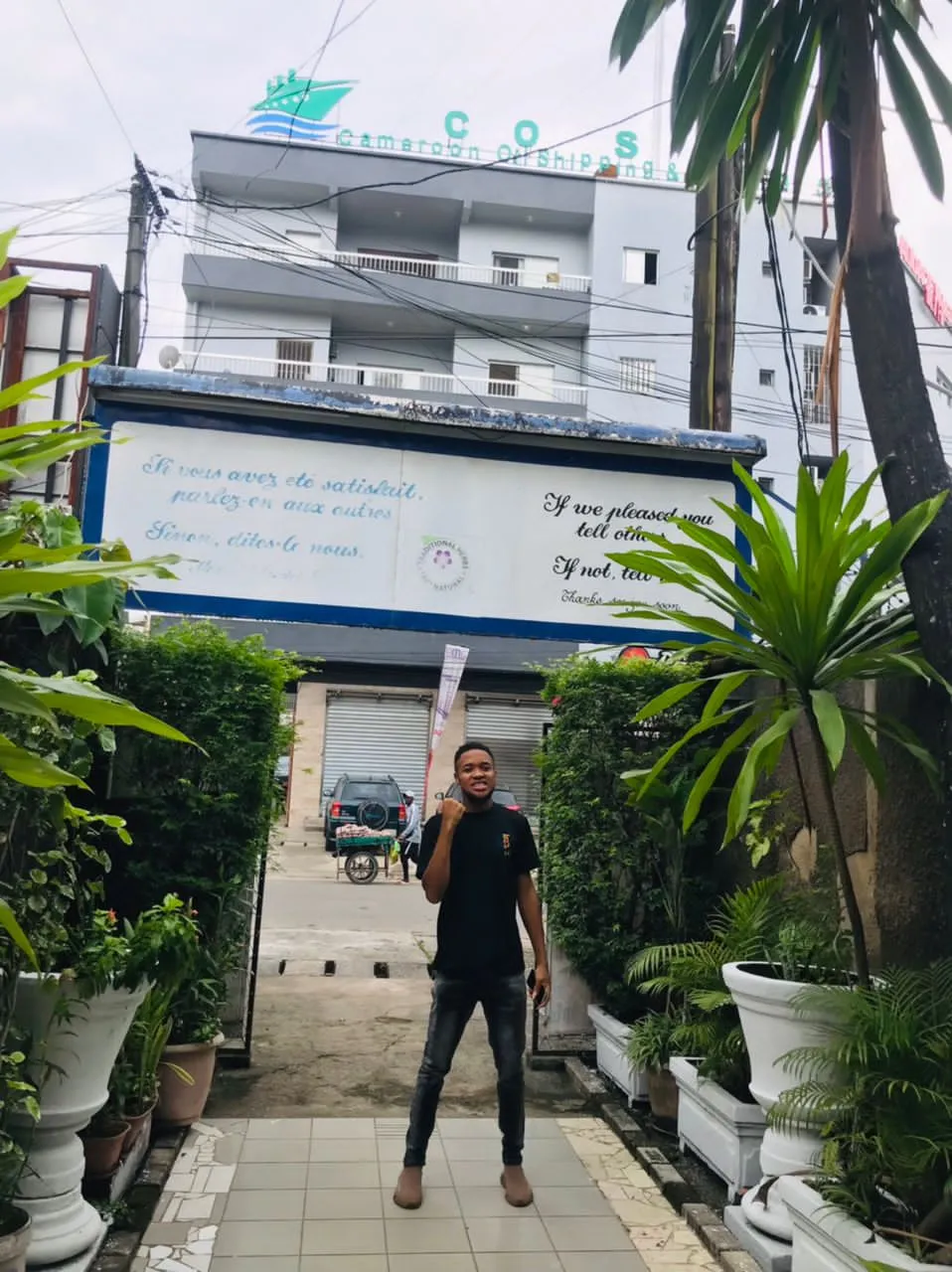 Nsom Emmanuel standing in a palm-lined office courtyard
