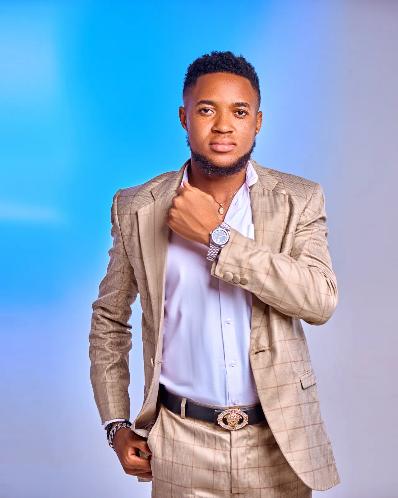 Nsom Emmanuel in a beige check suit against a blue studio backdrop
