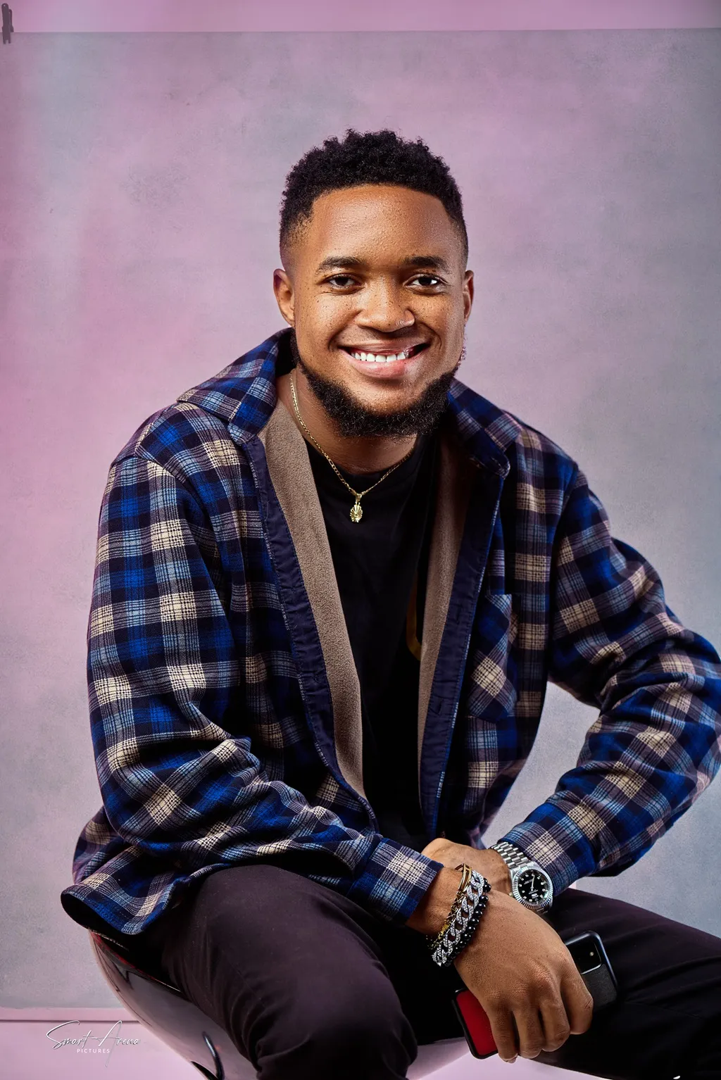 Nsom Emmanuel, smiling, seated in a plaid jacket against a soft studio backdrop