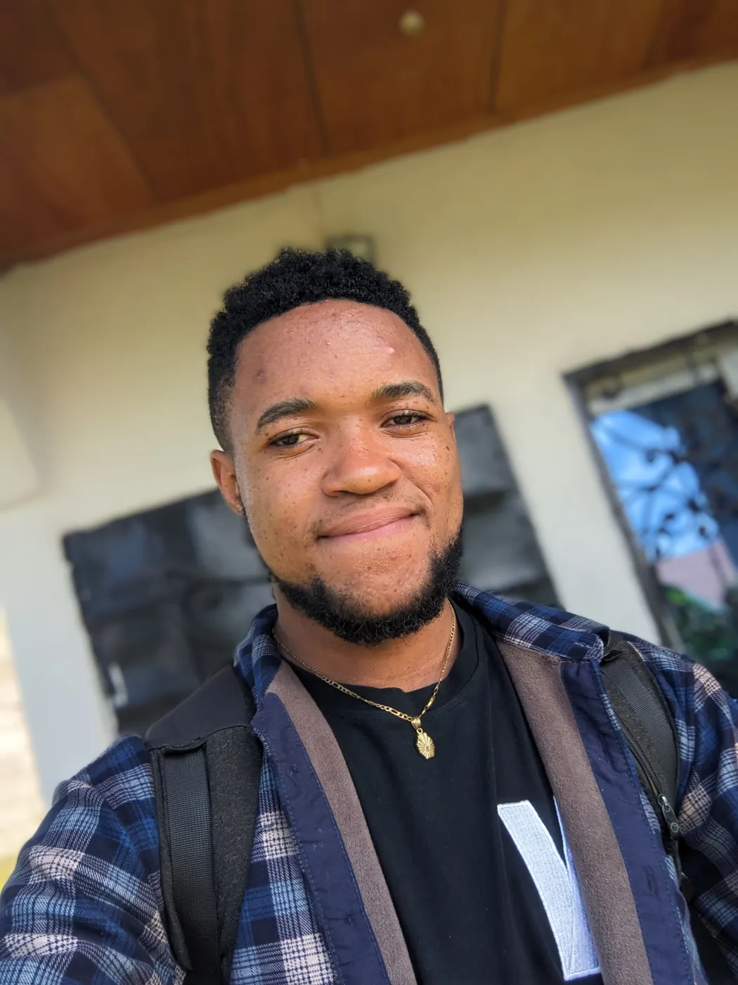 Nsom Emmanuel smiling in a plaid jacket, photographed indoors
