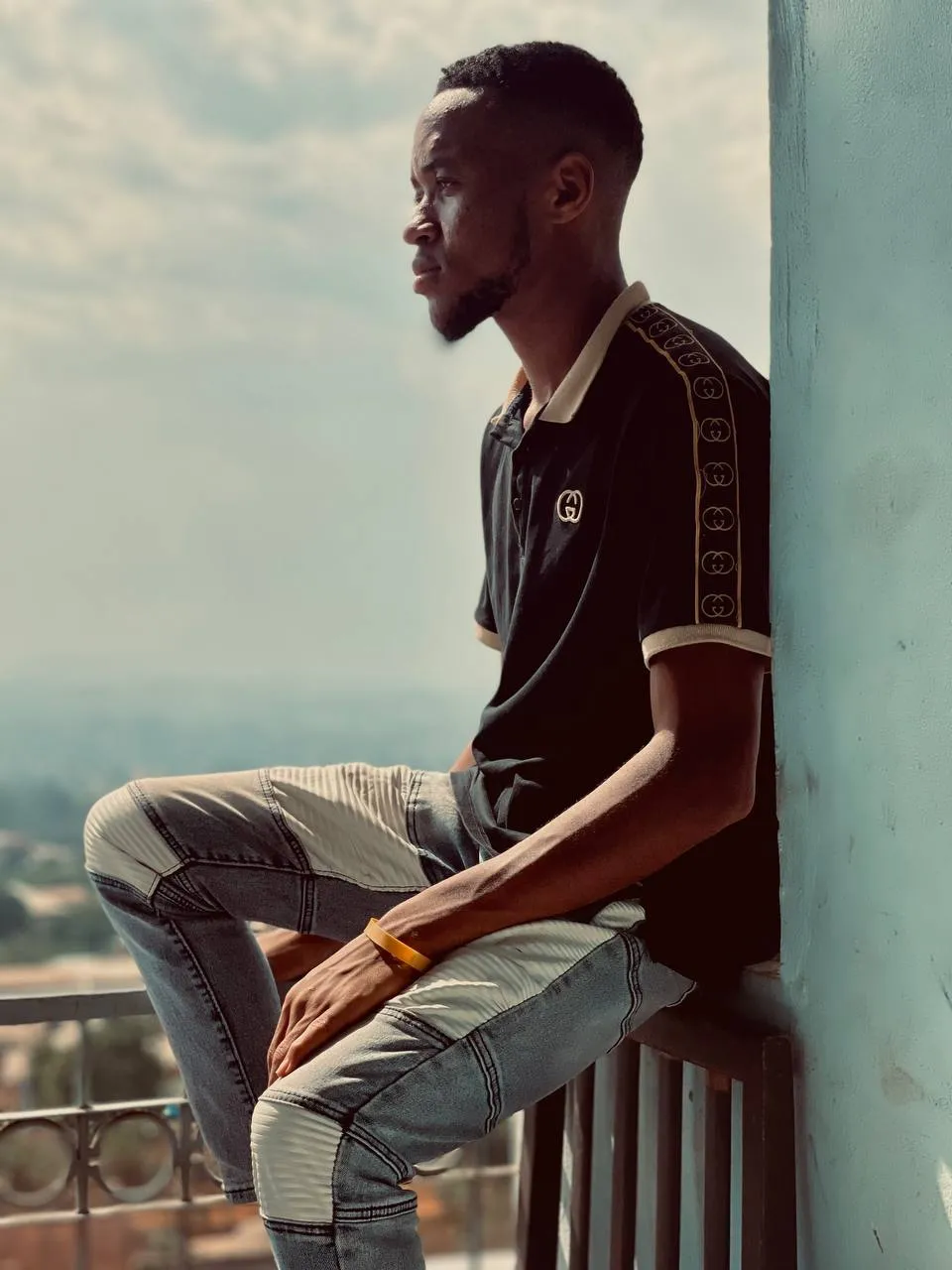 Nsom Emmanuel seated on a balcony ledge, looking out over the city