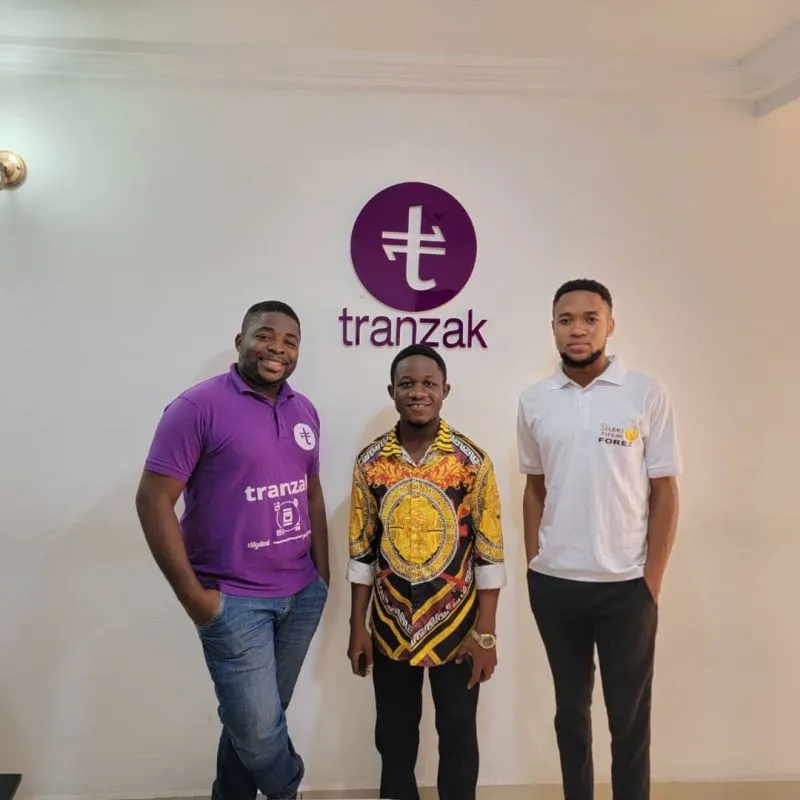 Three men standing in front of the Tranzak logo at the Tranzak office
