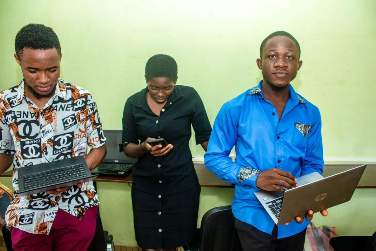 Nsom Emmanuel with two colleagues holding laptops in an office