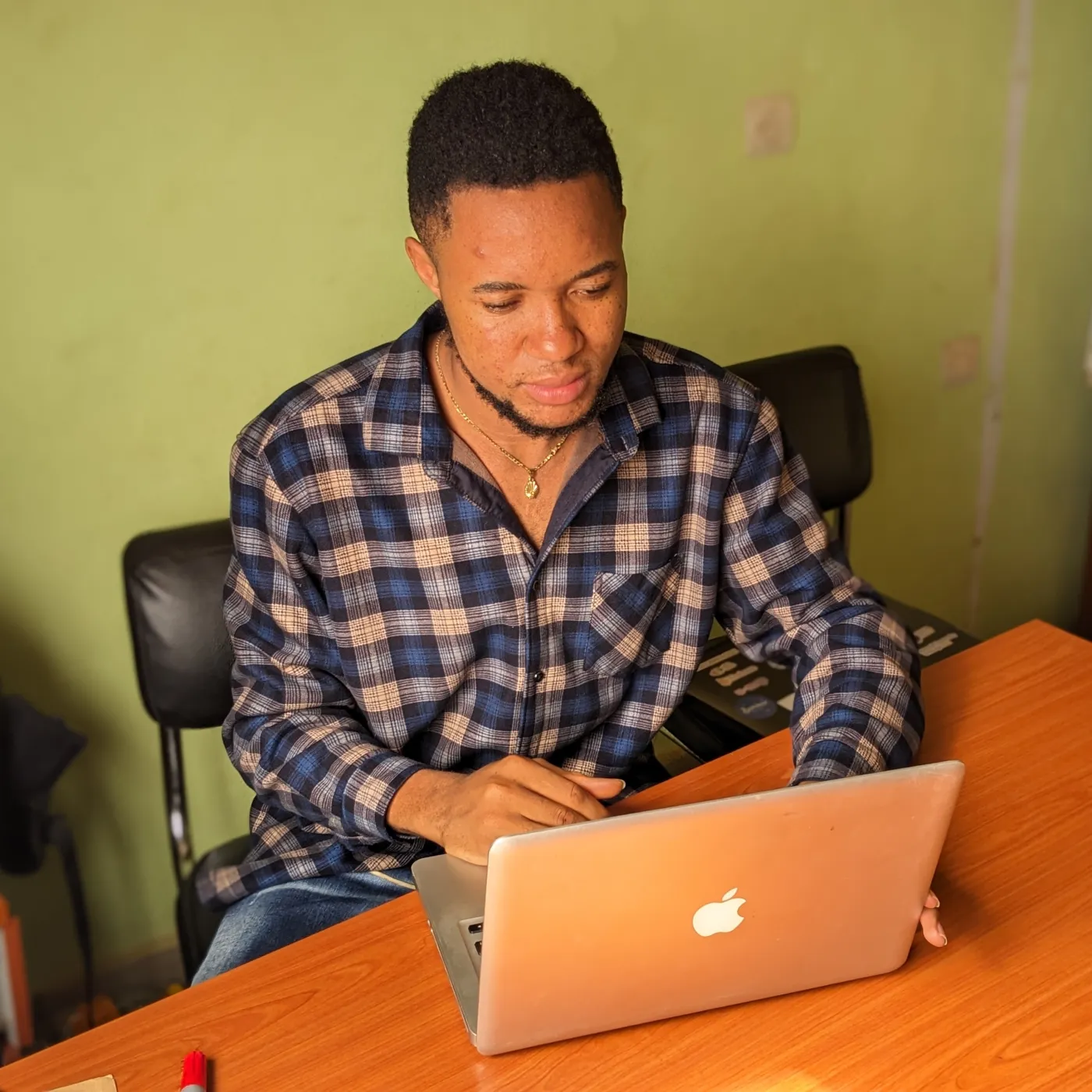 Nsom Emmanuel in a plaid shirt working on a laptop at his desk